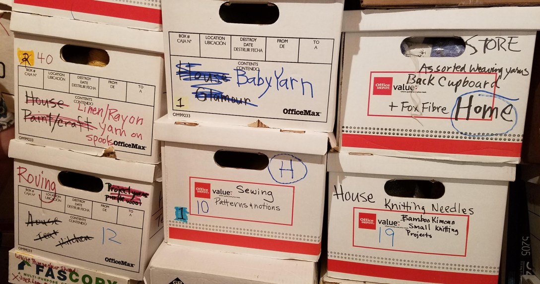 Three piles of white bankers boxes stacked four high, labeled "linen/rayon yarn', "baby yarn", "assorted weaving yarn" and "roving"